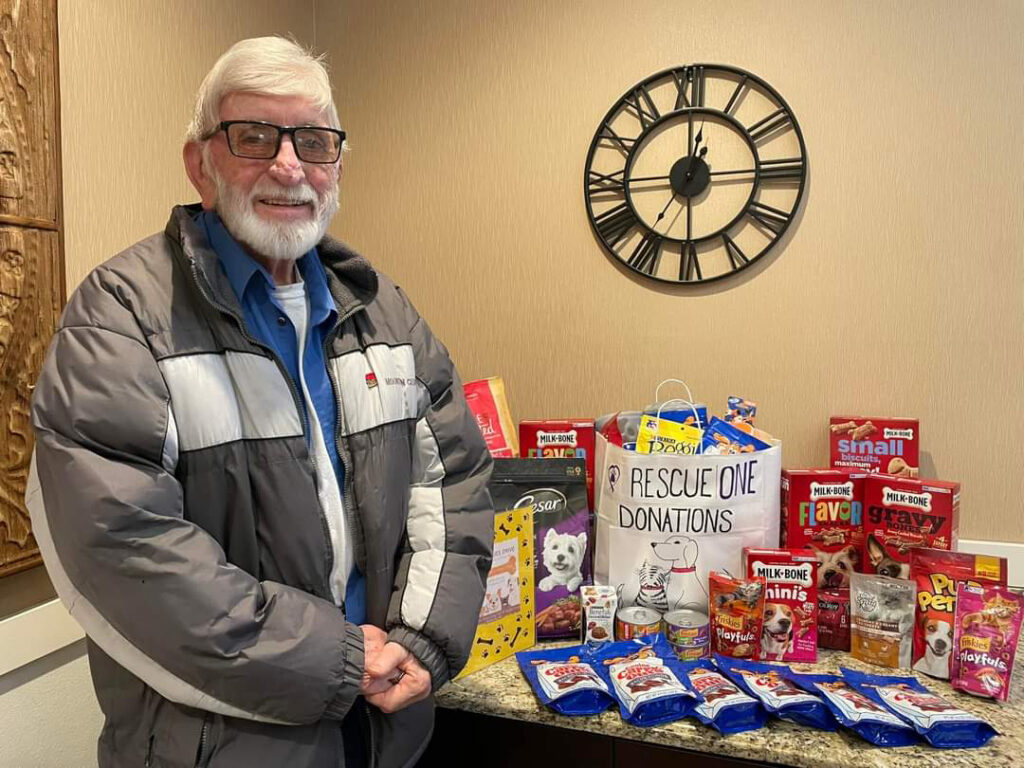 A smiling community senior resident proudly stands with donations for an animal shelter.
