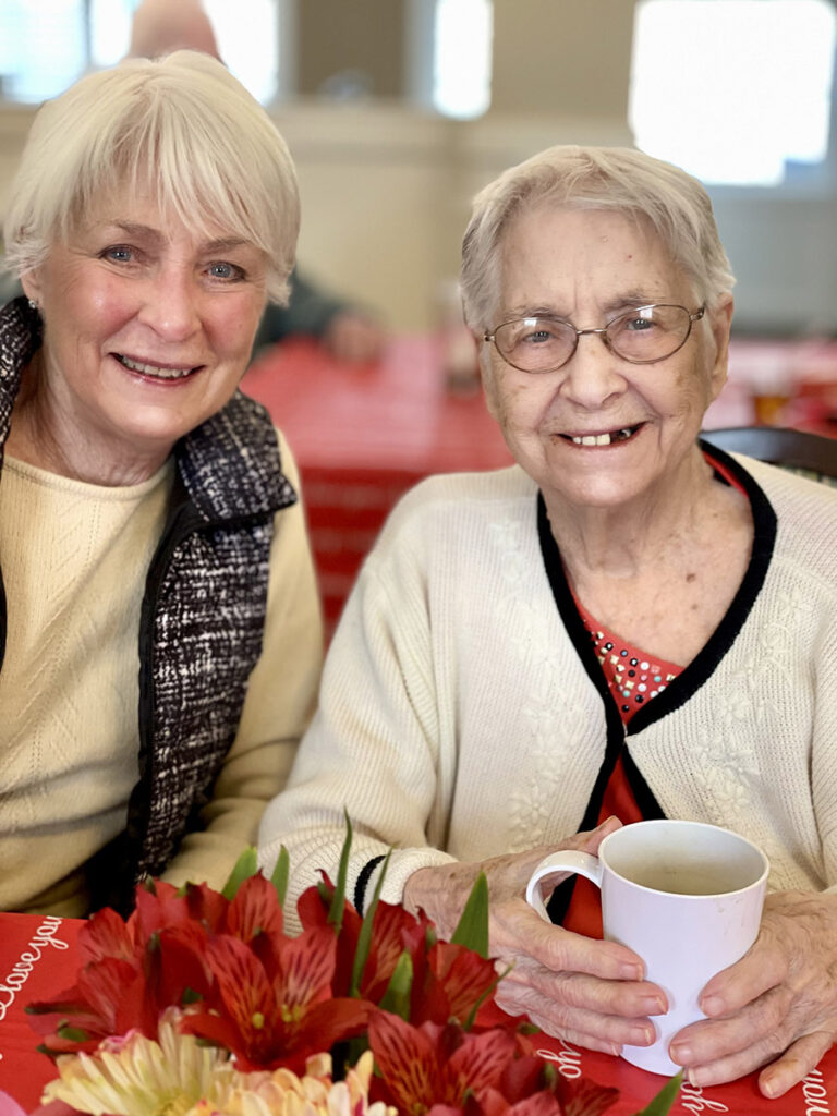 A volunteer and a memory care resident enjoy a heartwarming valentine brunch together, sharing smiles and creating cherished memories.