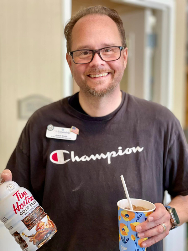 A smiling man at a senior living community holds a bottle of Tim Hortons cold brew coffee and a cup, embodying a relaxed and friendly atmosphere.