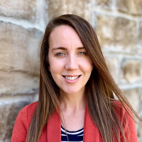 Lindsey Alarid, Senior Living Director at The Township Senior Living, smiles gently while standing outdoors in front of a stone wall wearing a coral blazer.