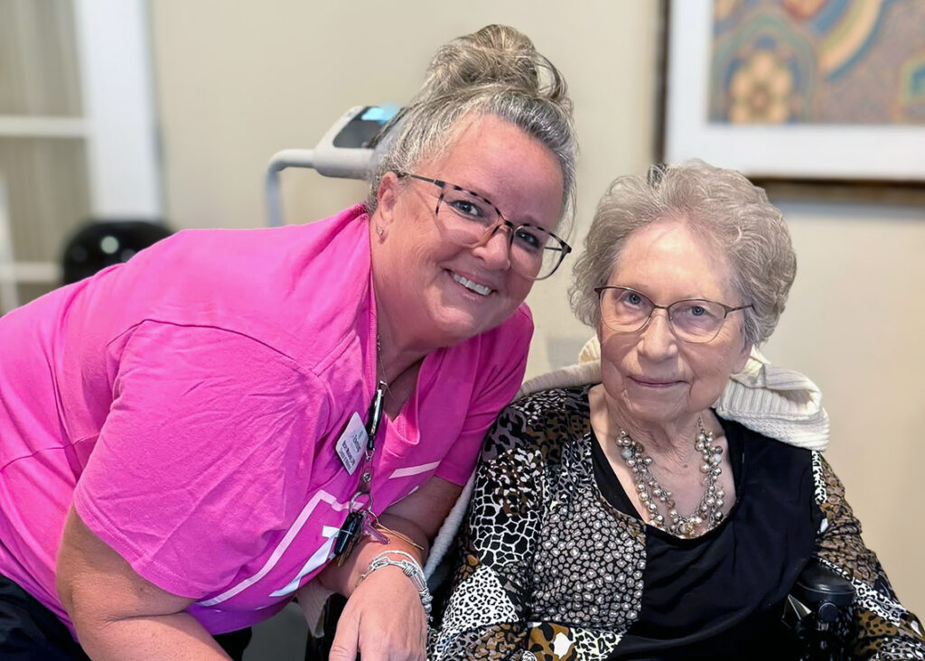 A team member in a bright pink shirt smiles with a senior resident at The Township.