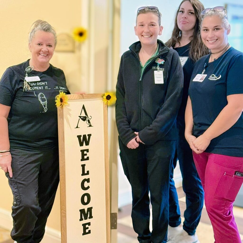 Team members smile beside a Welcome sign for Wellness Wednesday.
