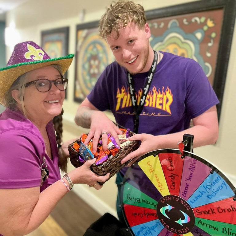 Two team members at The Township smile alongside a box of treats and a prize wheel.